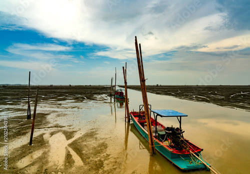 Fisherman's boat parked at coastal mud flat at tide. Landscape of sea and beautiful blue sky and white clouds. Mud beach.