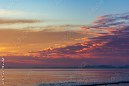 Dramatic vibrant orange sunrise sky with textured clouds over the ocean beach.