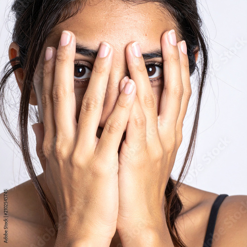 Mujer joven cubriéndose el rostro con las manos mirando de frente con expresión de miedo, ansiedad, inseguridad o sorpresa. Concepto de violencia de genero, salud mental, ansiedad y estrés