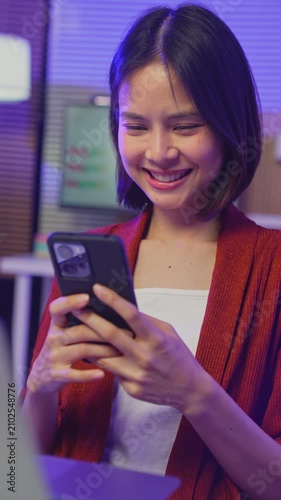 Young Asian woman using smartphone and smiling at mobile screen in home, digital communication and social media concept.
