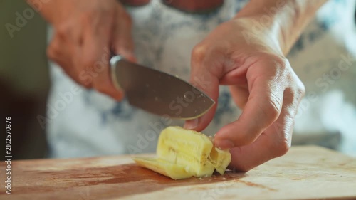 Woman’s hand slicing banana with kitchen knife on wooden cutting board