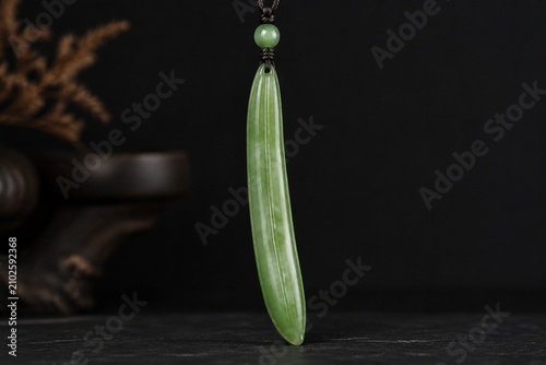 A slender green jade pendant shaped like a silique on a dark background.