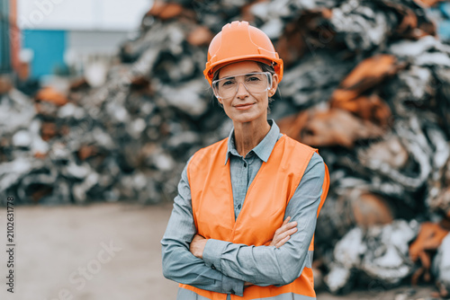 Female engineer safety helmet protective vest safety glasses recycling plant scrap metal industrial yard environmental worker waste management construction site Confident female engineer wearing