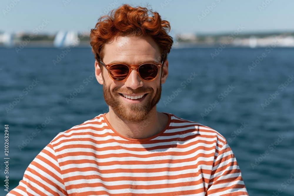 Fototapeta premium Smiling young man with sunglasses on a boat at sea in striped shirt summer portrait for lifestyle banner and social media background