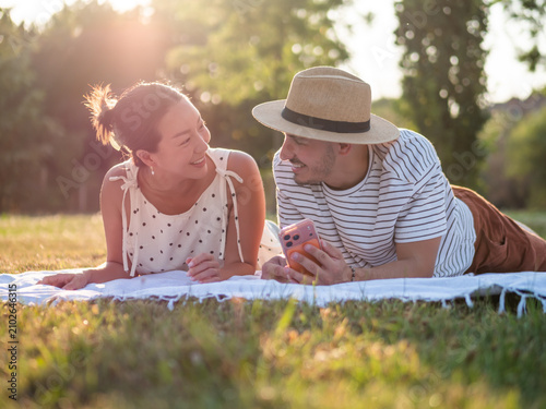 Happy couple spending time in park in summertime. They are using smartphone.