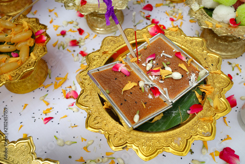 Thai custard dessert on golden color tray sprinkled with rose petals, jasmine flowers, and yellow marigold flowers, after the blessing ceremony.