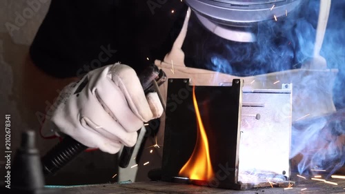 Welder operating stick electrode holder over metal structure with bright flame and light flash