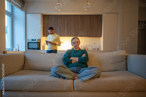 Obraz w ramie Emotional disconnection and ignorance in couple relationships, married partners ignoring each other, angry wife sitting on couch while uninterested manipulative husband wasting time on smartphone.