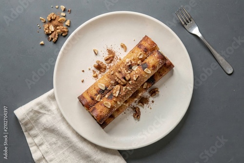 Plate with Trdelnik, grilled pastry coated with sugar walnuts, surrounded by crunchy walnuts. Concept of dessert styling featuring golden-brown toasted notes and rich textures.