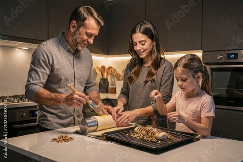 Family of three enjoying Trdelnik preparation in modern kitchen, smiling together while making grilled pastry coated with sugar walnuts. Concept of family bonding and baking joy.