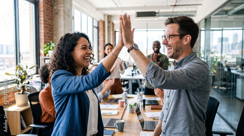 Business colleagues giving high five during office meeting celebration of project success.