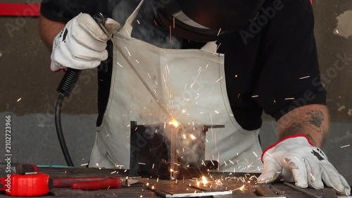 Selective focus on welder hands holding electrode rod with sparks flying in a garage