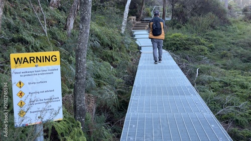 Foto Hiker Walking on Steel Grated Boardwalk Path Through Lush Forest