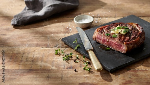 Juicy grilled ribeye steak with melting butter and herbs on full hd 4k stock image download black slate