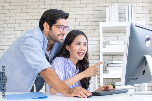 Business couple working, communicating while sitting at the home office desk together. Cheerful couple, calm asian woman and caucasian man working at home with laptop together.