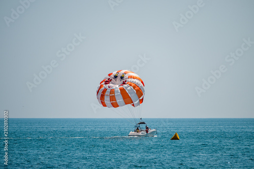 Obraz na plátně a bright orange and white striped parasail gliding above a vibrant blue ocean, towed by a small white motorboat under a clear, cloudless sky