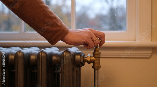 Person adjusting radiator valve, regulating home temperature, managing heating system, saving energy and staying warm