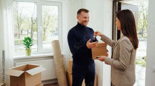 Smiling couple receiving house keys from realtor, moving into bright new home, conveying happiness and settling in concept