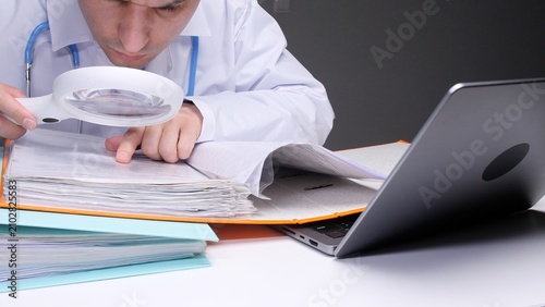 Fotografía Doctor in a white coat scrutinizing medical records with a magnifying glass, per