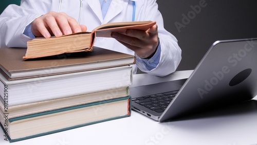 Schilderij op canvas Medical professional in a lab coat and stethoscope studying an open book and sta