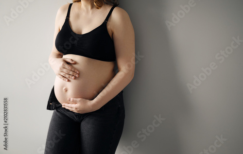 Pregnant woman gently holding her bare belly. Commercial concept of prenatal care, maternity health, expecting a baby, family planning, and maternal wellness.