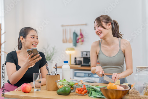 Asian woman kitchen cooking vegetable friend smiling phone healthy food home joyful friends prepare fresh vegetable meal in bright kitchen