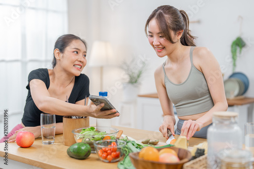 Woman kitchen cooking vegetable smartphone smile home food fruit, two Asian woman prepare fresh vegetable and fruit in bright home kitchen while smiling and sharing smartphone