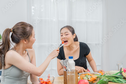 Woman friend cooking kitchen food vegetable salad happy lifestyle home woman feeding friend with vegetable bright kitchen, laughing during healthy meal preparation with fresh ingredient, utensil