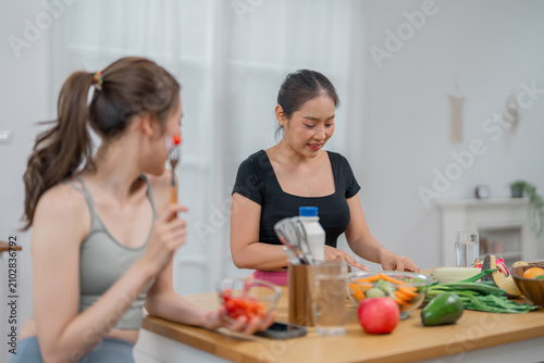 Woman kitchen vegetable cooking food healthy meal preparation Young woman preparing fresh vegetable while friend eats at home kitchen table with fruit utensil glass and relaxed lifestyle scene