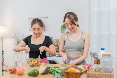 Woman cooking kitchen vegetable salad food healthy home smiling lifestyle, two young women prepare fresh salad together bright home kitchen with vegetable, fruit, cutting board, and cheerful