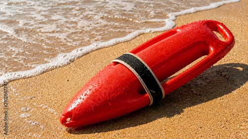 Red lifeguard rescue torpedo buoy resting on wet sand at the beach