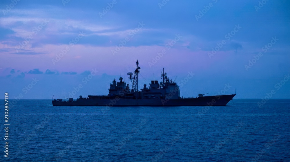 Fototapeta premium Silhouetted warship glides across calm ocean waters