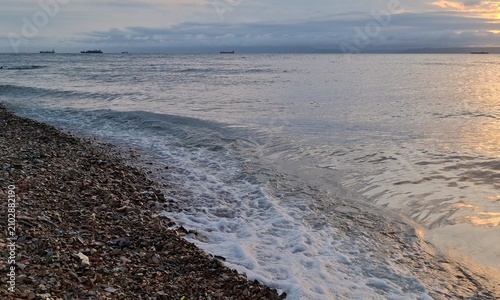 Foto Pebble beach with soft sea foam waves washing the shore under an overcast sky