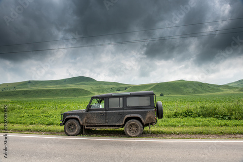 Quadro su tela Overcast Sky Over Mud-Covered Land Rover Defender on Rural Road, Green Rolling H