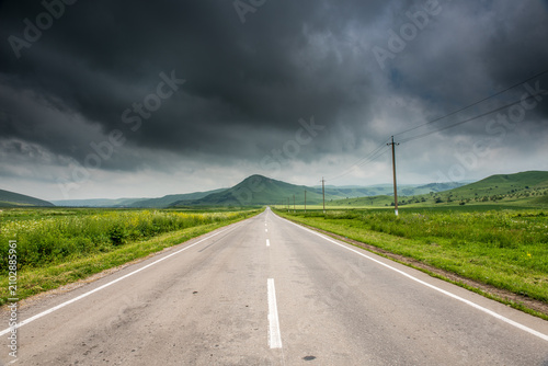 Tableau sur toile Dramatic Storm Clouds Over Empty Rural Road Through Green Hills, Caucasus Region