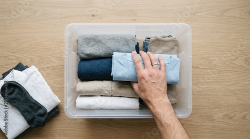 Person Organizing Folded Clothes in Plastic Storage Bin for Minimalist Closet Organization and Decluttering Project