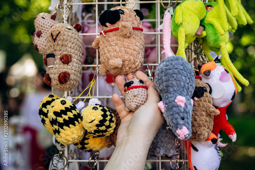 Woman choosing handmade plush animal keychain at craft market.