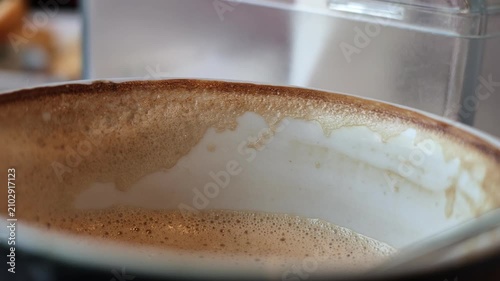 Macro slow motion shot tracking the thick brown foam ring stain left on the inner rim of a white ceramic cappuccino cup as it tilts.
