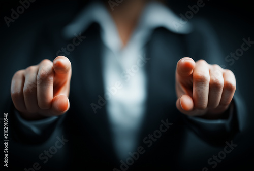 A close-up of a businesswoman pointing directly toward the viewer with both hands, symbolizing choice, selection, engagement, and interactive decision-making against a dark background.