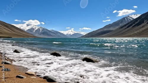 Beautiful mountain lake with waves and snow peaks under a blue sky