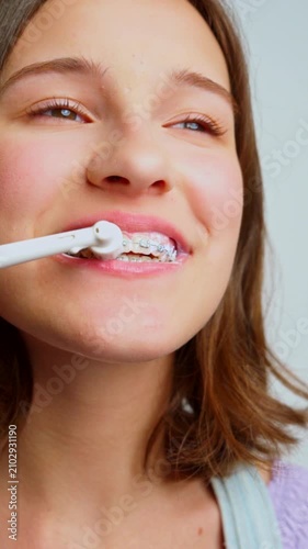 teenage girl brushing teeth with braces using electric toothbrush showing orthodontic dental care routine closeup macro shot of metal brackets and foam toothpaste cleaning process on young smile