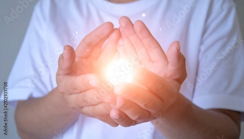 Person cupping hands around radiant golden light orb.