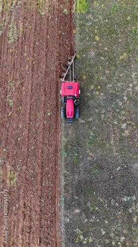 a red tractor plowing a field with a plow, drone view