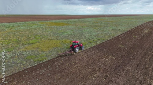 a red tractor plowing a field with a plow, drone view