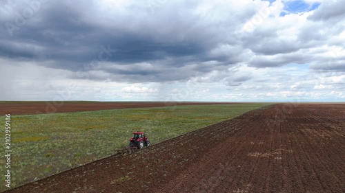 a red tractor plowing a field with a plow, drone view