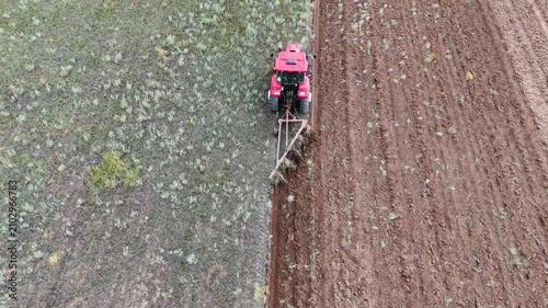 a red tractor plowing a field with a plow, drone view