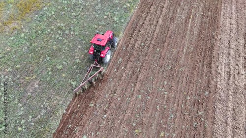 a red tractor plowing a field with a plow, drone view