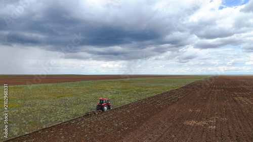 Fotografía a red tractor plowing a field with a plow, drone view