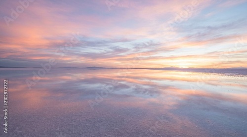 Pastel sunset reflects across a vast calm salt flat with distant mountains on the horizon, ideal for travel, wellness, or nature campaign backgrounds.