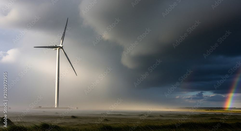 Obraz premium Wind turbine under stormy sky with rainbow, renewable energy and nature's power.